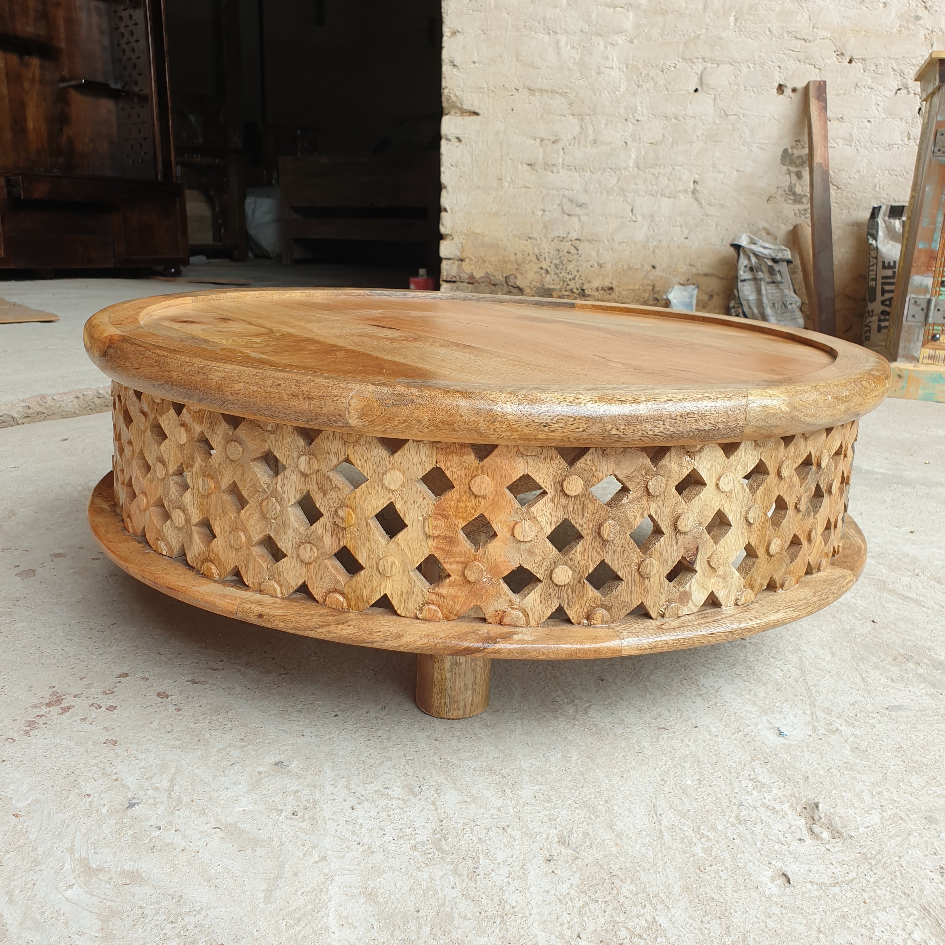 Low round mango wood coffee table with geometric diamond openwork carving, natural timber finish and raised tabletop edge.