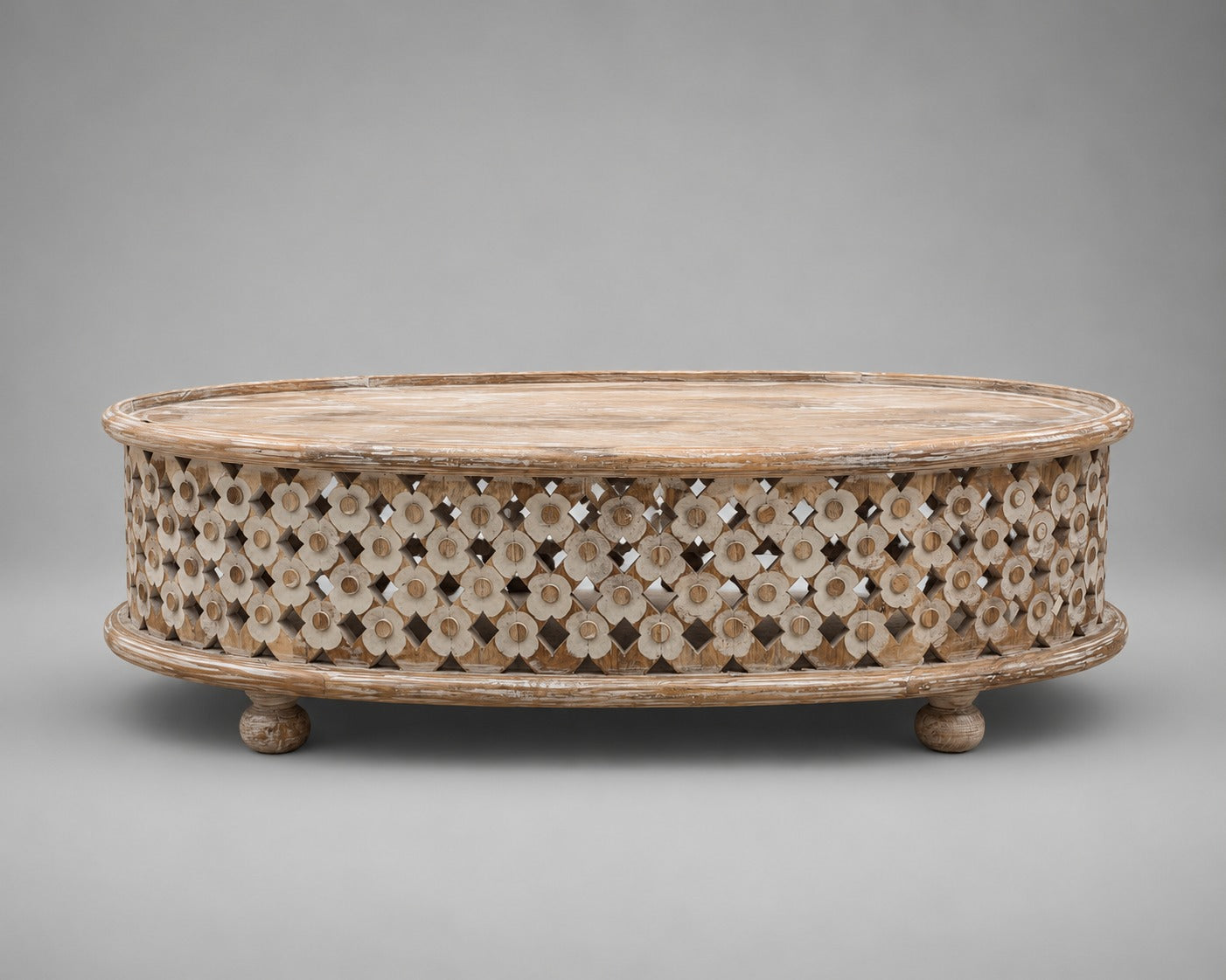An oval wooden coffee table with a carved, openwork floral pattern on the sides and small round feet, shown against a neutral gray background.