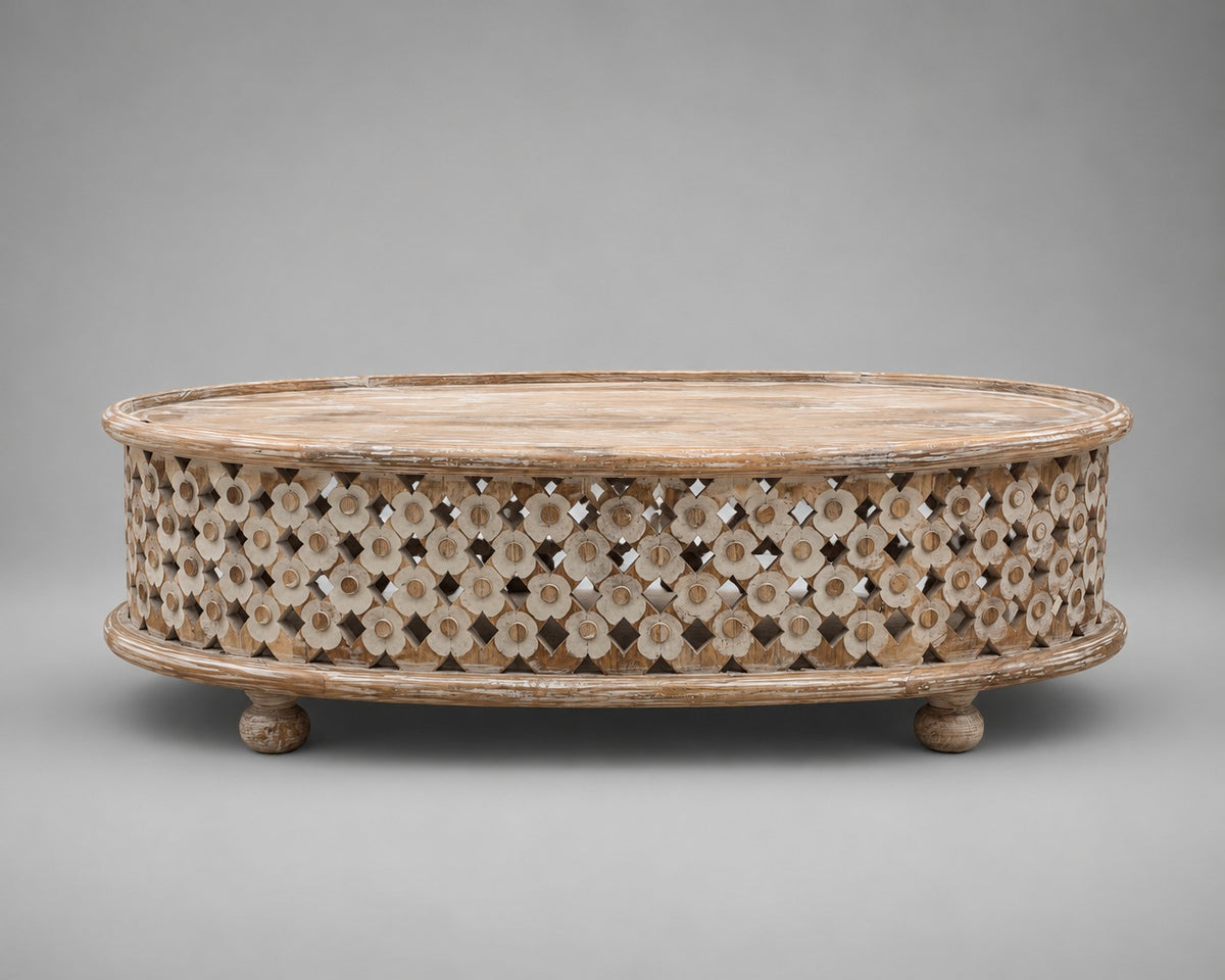 An oval wooden coffee table with a carved, openwork floral pattern on the sides and small round feet, shown against a neutral gray background.