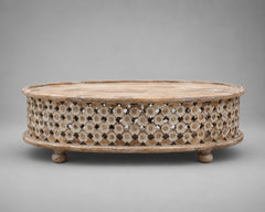An oval wooden coffee table with a carved, openwork floral pattern on the sides and small round feet, shown against a neutral gray background.