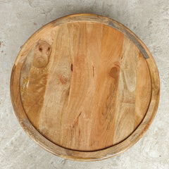 A round wooden serving board or tray with a raised rim, made from natural wood with visible grain, knots, and warm tan and brown tones, photographed from directly above on a light gray textured surface.