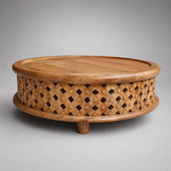 A round wooden coffee table with a carved lattice pattern on the sides and a single short leg, photographed on a neutral gray background.