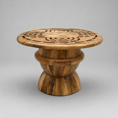 A round wooden side table with a carved geometric pattern on the top and a tiered pedestal base, shown on a neutral gray background.