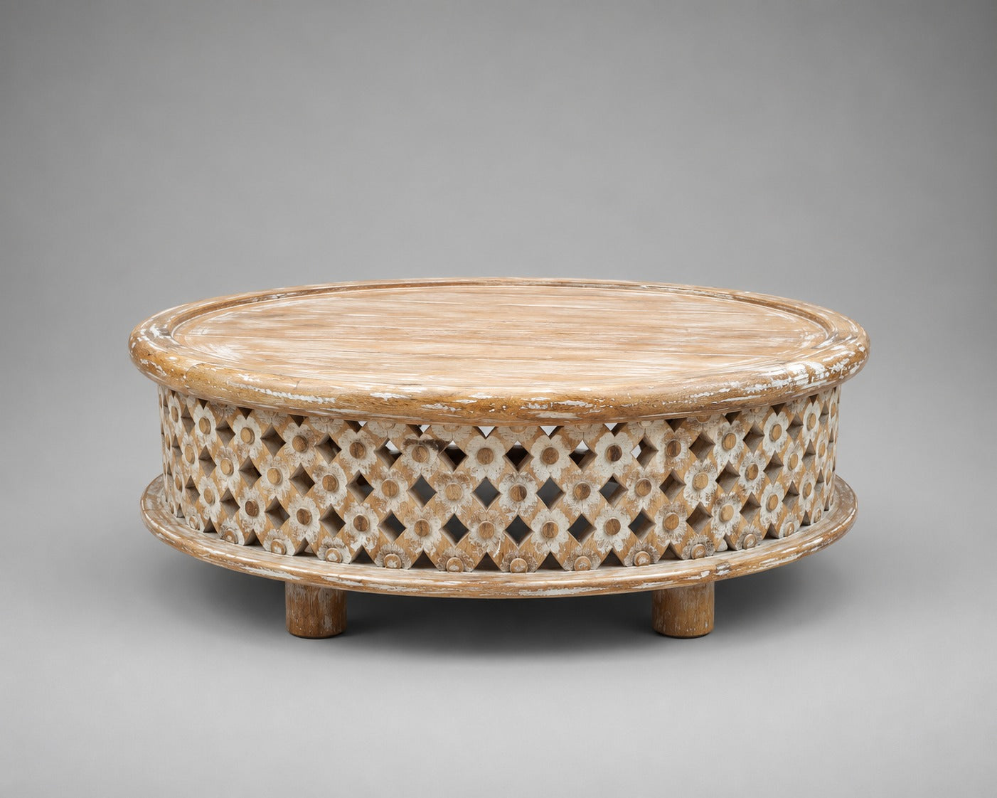 Whitewashed low round mango wood coffee table with geometric floral lattice carving and raised circular tabletop.