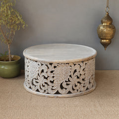 Decorative wooden table with intricate carvings on a textured surface with a plant and hanging ornament.